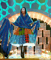 a woman in a colorful dress is standing in front of a neon sign that says t4yce