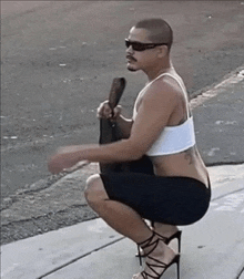 a man squatting down wearing high heels and a white tank top .