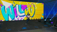 a woman is dancing in front of a large screen with the word wow on it
