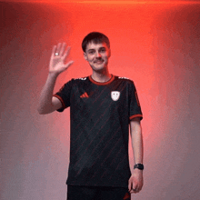 a man wearing a black adidas shirt is waving his hand