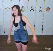 a woman in overalls stands in front of a wall with balloons that spell out the word " car "