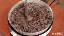 a pan of ground beef is being stirred with a spoon and the words made in animatica are visible in the corner