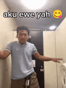 a man in a blue shirt is dancing in a public restroom with the words aku ewe yah written above him