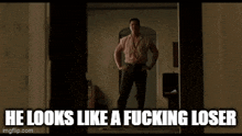 a man is standing in a doorway with his hands on his hips and the caption he looks like a fucking loser .