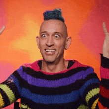 a man wearing a rainbow striped sweater is smiling with his hands in the air