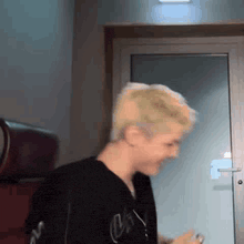 a man with blonde hair is standing in front of a glass door and looking at his phone .