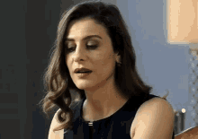 a woman in a black dress is sitting in front of a lamp and looking down
