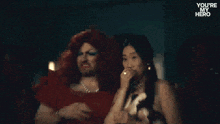 a man in a drag queen costume is standing next to a woman with the words you 're my hero written on the bottom