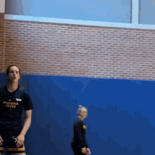 a woman wearing a shirt that says indiana fever stands in front of a blue wall