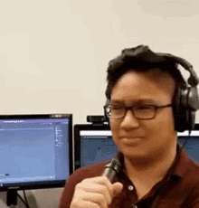 a man wearing headphones is holding a microphone in front of two computer monitors .