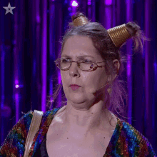 a woman wearing glasses and a gold cone in her hair stands in front of a purple background with a star on it