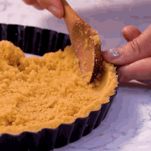 a person is using a wooden spoon to spread a crumb crust into a pan