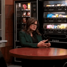 a woman is sitting at a table in front of a vending machine that says push