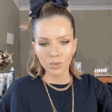 a woman wearing a black sweater and a gold necklace is making a funny face .