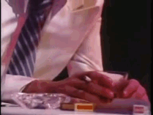 a man in a suit and tie is smoking a cigarette next to an ashtray