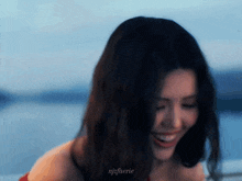 a woman in a red dress is smiling and looking at the camera while standing next to a body of water .