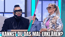 a man and a woman are sitting next to each other on a stage and the woman is wearing glasses .