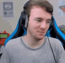 a man wearing headphones and a grey shirt is sitting in a blue chair .
