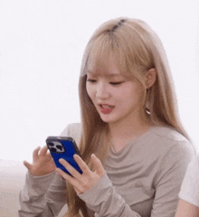 a woman with blonde hair is holding a cell phone in her hand .