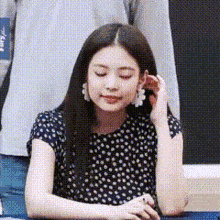 a woman in a black polka dot shirt is sitting at a table with her eyes closed and touching her ear .