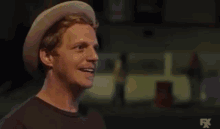 a man wearing a hat and smiling is standing in front of a fire .