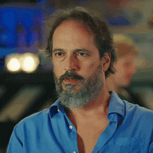 a man with a beard wearing a blue shirt looks at the camera