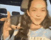 a woman is sitting in the back seat of a car making a peace sign with her hand .