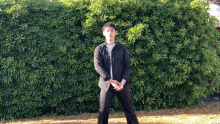 a man in a black shirt stands in front of a lush green bush