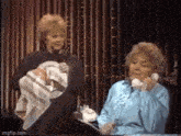 two women are standing next to each other on a stage and one is talking on a phone .