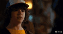 a young boy wearing a hat and a yellow t-shirt says what