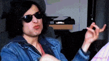 a man wearing sunglasses and a denim jacket is making a face