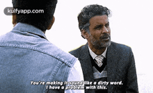 a man in a suit and tie is talking to another man in a denim shirt .