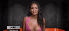 a woman in a pink bikini top is sitting in front of a black wall .