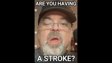 a man with a beard wearing glasses and a hat says are you having a stroke