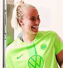 a woman in a green shirt with a vw logo on it is smiling .