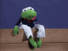 a kermit the frog is sitting on a wooden ledge .