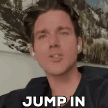 a man wearing ear buds says jump in while sitting in front of a painting .