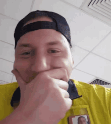 a man wearing a yellow shirt and a black hat is covering his mouth with his hands