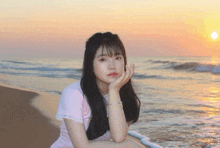 a girl in a pink shirt sits on a beach at sunset