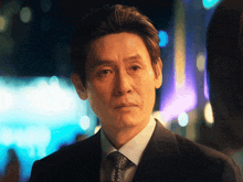 a man in a suit and tie looks at the camera with a blurry background