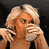 a woman is drinking from a glass while wearing a necklace with the word cakes on it .