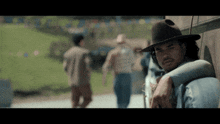 a man in a cowboy hat leans on a car