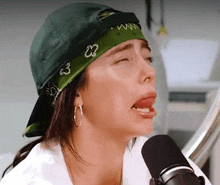 a woman wearing a green bandana and a baseball cap is making a funny face in front of a microphone .