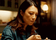 a woman in a blue shirt is sitting at a table eating with chopsticks