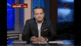 a man sitting at a desk with a sign that says memri-tv