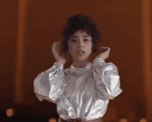 a woman with curly hair is wearing a silver top and making a face .