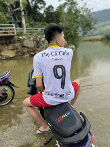 a man is sitting on a motorcycle wearing a white shirt with the number 9 on it
