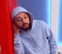 a man with a beard wearing a hoodie and headphones leaning against a wall .