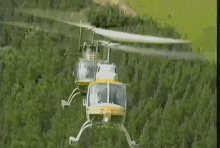 a helicopter is flying over a green field with trees in the background