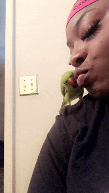 a woman wearing a pink headband with the word go on it kisses a green parrot on her shoulder